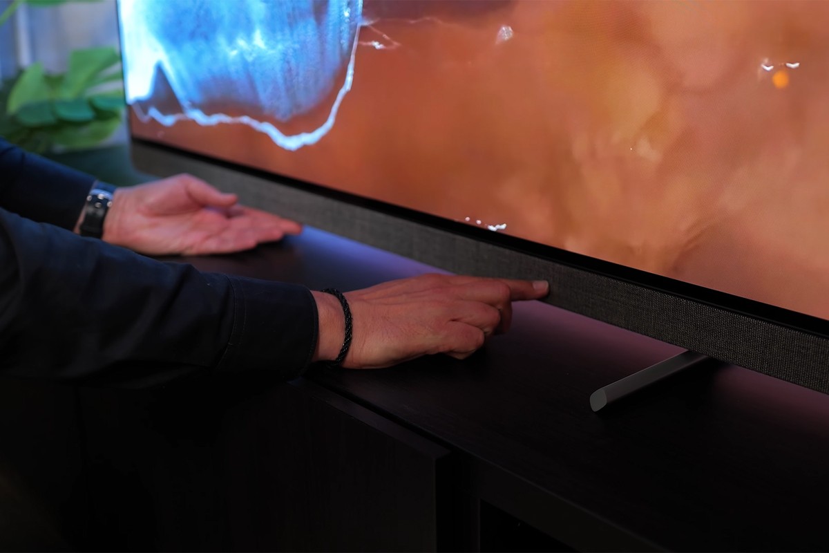 Philips OLED Een persoon wijst met beide handen naar de stoffen speakerafwerking aan de onderkant van het scherm van de Philips OLED+