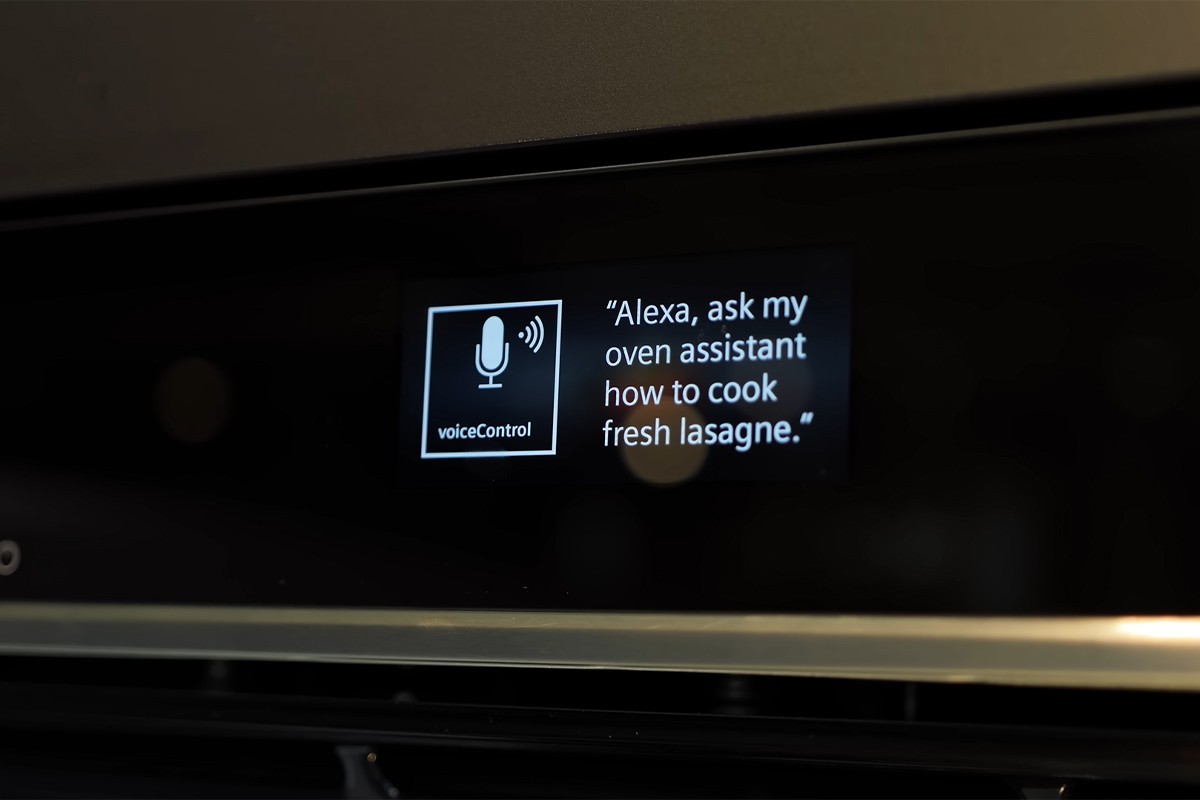 Een display van een Siemens oven waarop een melding staat met spraakbediening: “Alexa, ask my oven assistant how to cook fresh lasagne.”; links van de tekst staat een pictogram van een microfoon met de aanduiding “voiceControl”.