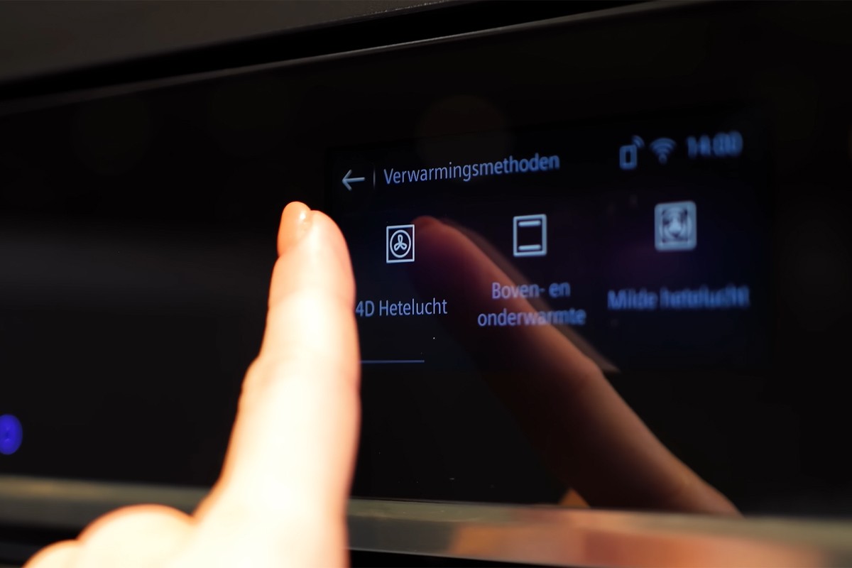 Een close-up van het touchscreen van een Siemens oven, waarop een vinger het menu “Verwarmingsmethoden” bedient; zichtbaar zijn opties zoals “4D Hetelucht”, “Boven- en onderwarmte” en “Milde hetelucht”, met bijbehorende pictogrammen.
