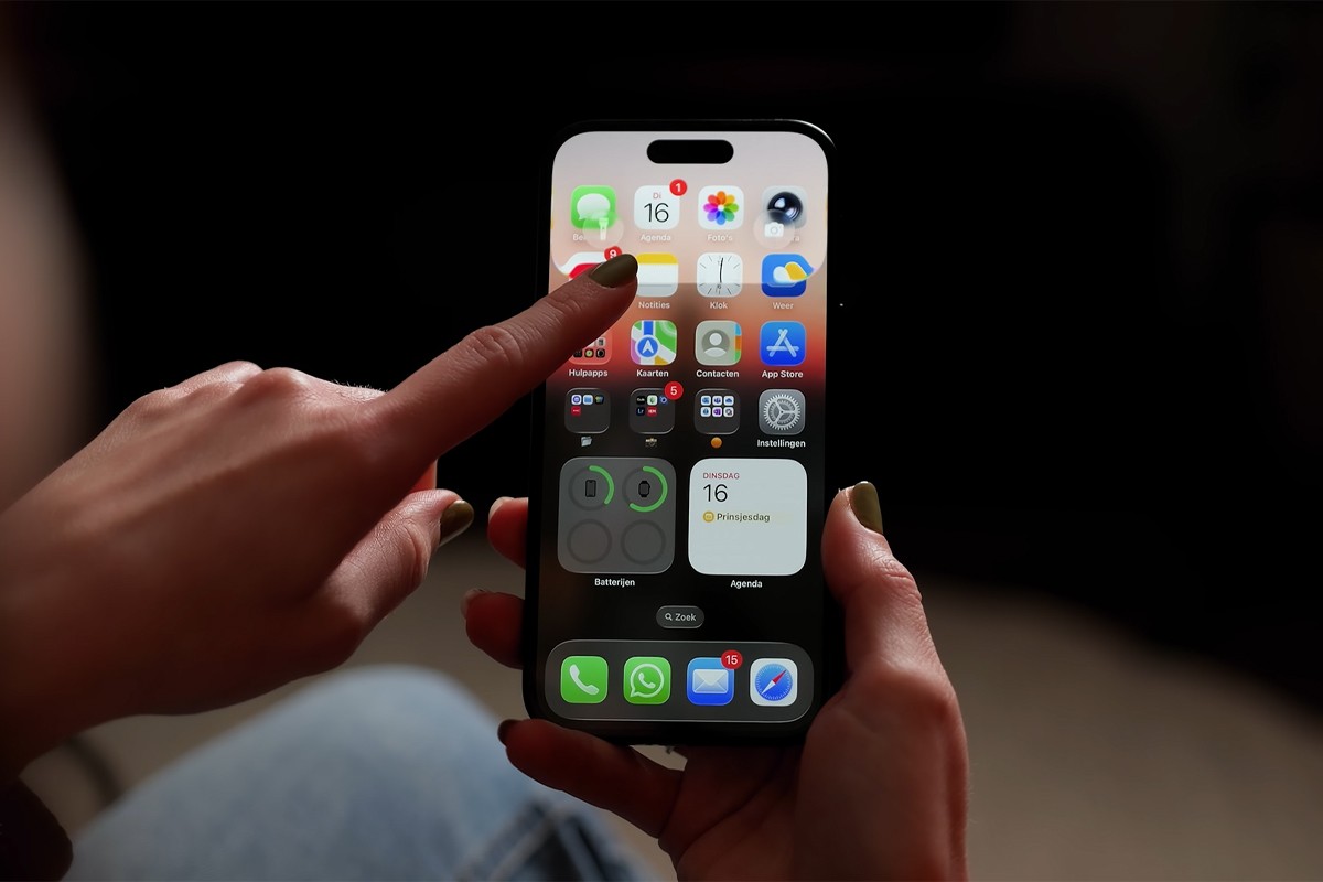 Persoon houdt een iPhone vast en swipet met vinger het notificatiescherm omlaag waarbij het effect van Liquid Glass goed te zien is.