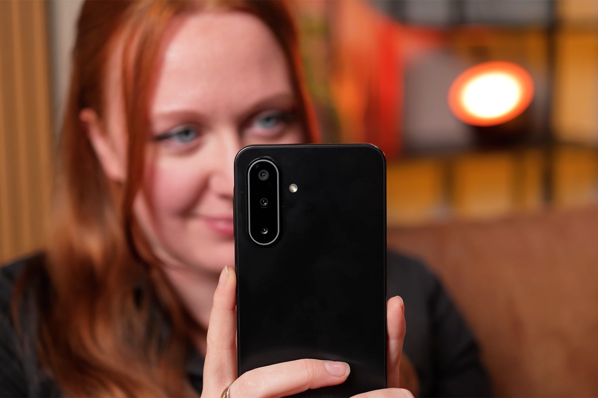 Samsung Galaxy A17 Een vrouw houdt een Samsung Galaxy A17-smartphone voor zich, met de achterkant naar de camera gericht; de telefoon heeft drie verticale cameralenzen en een LED-flitser in een ovale cameramodule