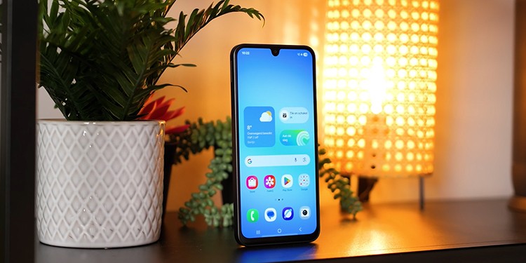 Samsung Galaxy A17 staat rechtop op een plank naast een witte plantenpot en een sfeervolle tafellamp