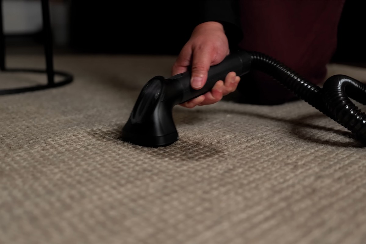 Eufy Omni E28 vlekkenreiniger Een persoon gebruikt de vlekkenreiniger van de Eufy Omni E28 om een vlek op een beige tapijt te reinigen