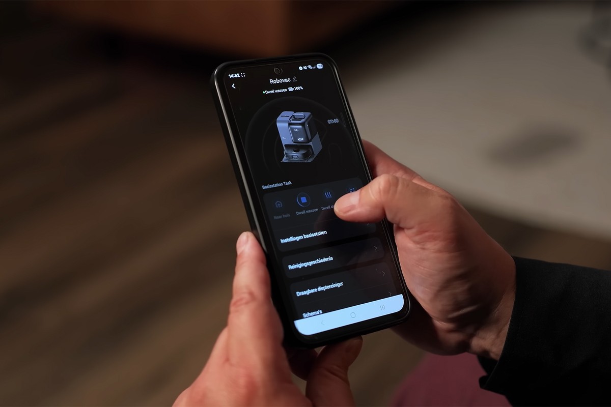 Eufy Omni E28 appbediening Een persoon bedient een robotstofzuiger via een smartphone-app.