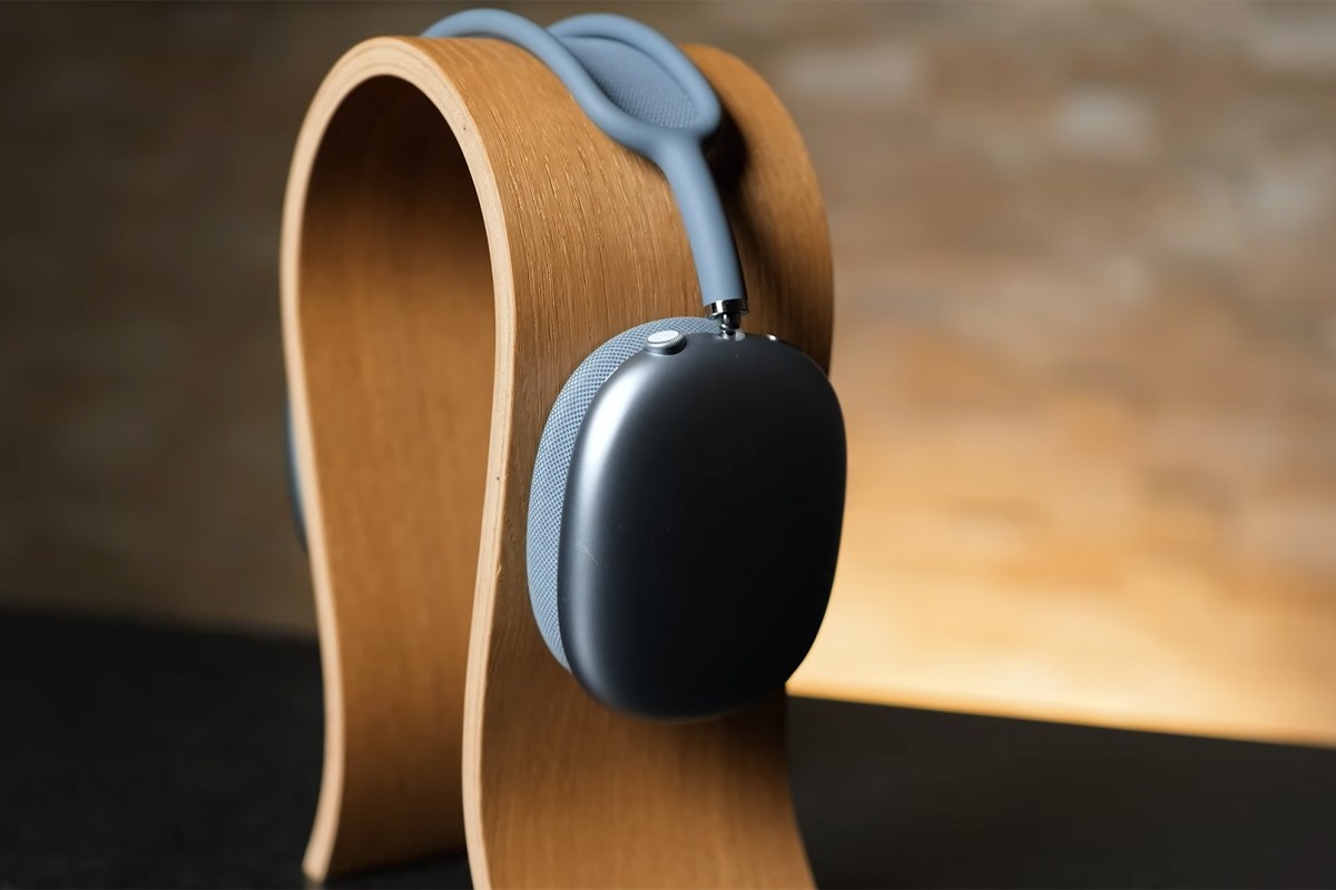 Een close-up van een blauwe Apple AirPods Max-koptelefoon, rustend op een houten hoofdtelefoonstandaard.