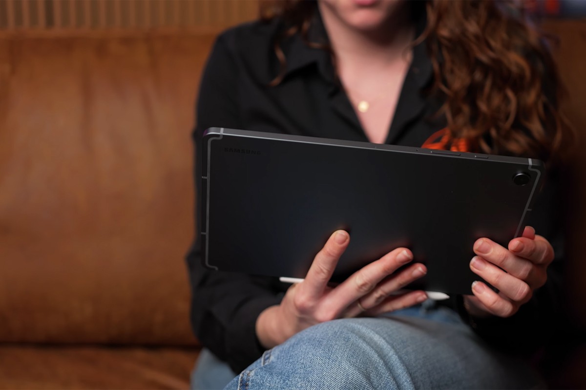 Vrouw zit op een bank en houdt de Samsung Galaxy Tab S10 Lite horizontaal vast, met de achterkant van de tablet in beeld.