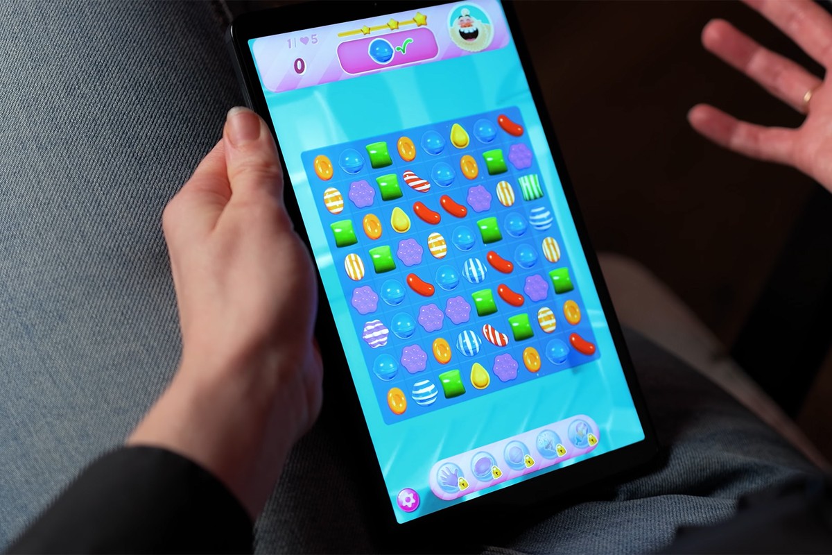 Een persoon houdt de Samsung Galaxy Tab A11-tablet vast waarop het spel Candy Crush wordt gespeeld; op het scherm zijn kleurrijke snoepjes te zien in verschillende vormen en kleuren, gerangschikt in een rastervormig speelveld.
