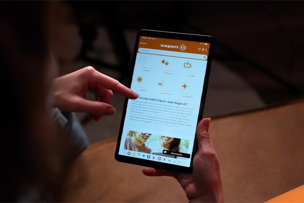 Een persoon houdt een Samsung Galaxy Tab A11-tablet in de hand en navigeert met de wijsvinger over de website van Expert.nl, waarop een pagina zichtbaar is over het kiezen van een nieuwe tablet; bovenaan staat het oranje Expert-logo en diverse icoontjes.