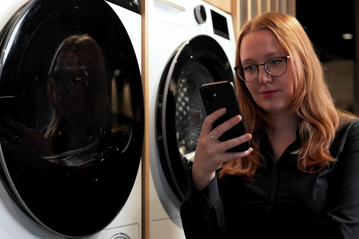 Een vrouw staat voor twee Whirlpool-wasmachines en kijkt geconcentreerd naar haar smartphone waarop ze de HomeWhiz-app gebruikt.