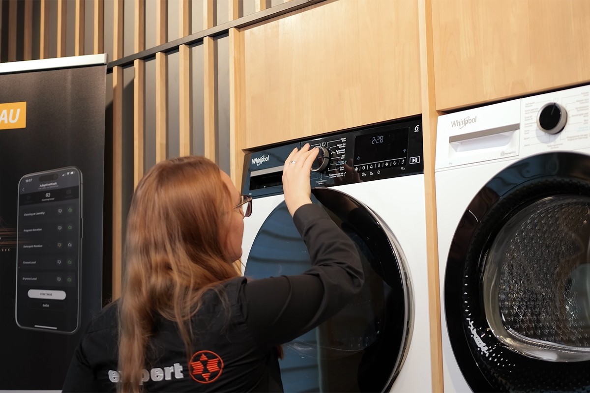 Een medewerkster van Expert bedient een Whirlpool-droger. Ze draait aan de centrale programmaknop van het apparaat.