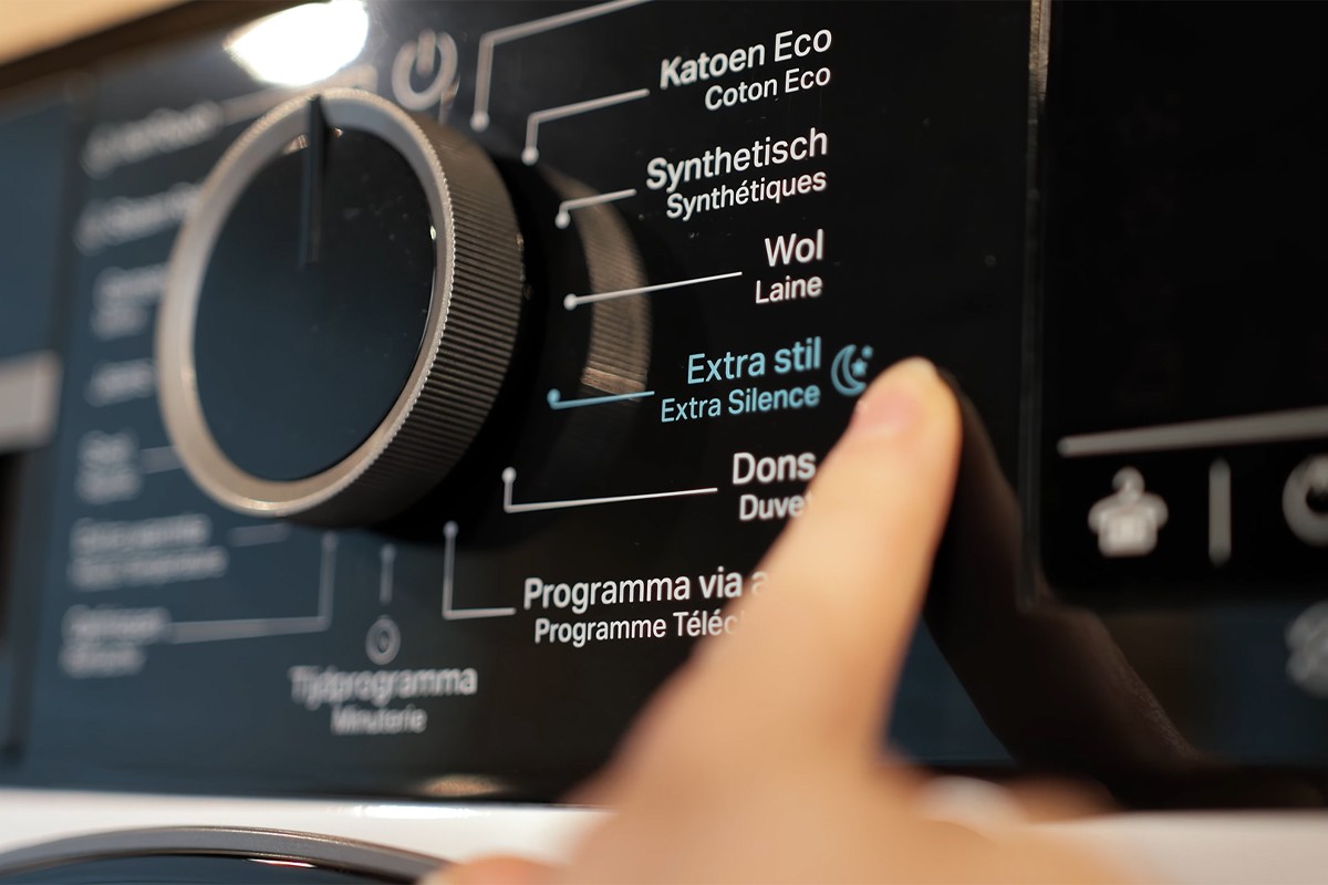 Een vinger wijst naar de optie ‘Extra stil’ op het bedieningspaneel van een Whirlpool-droger; het programma is gemarkeerd met blauwe letters en een maansymbool.