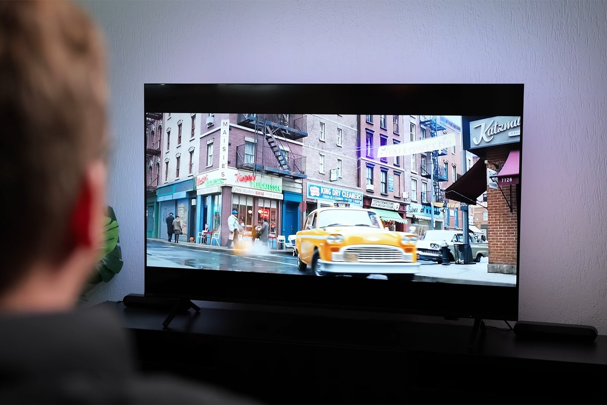 Persoon kijkt naar televisie waarop een gele taxi te zien is die de hoek om scheurt