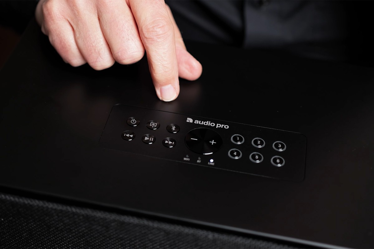 Close-up van de fysieke knoppen bovenop de Audio Pro C10 MKII waarbij een persoon wijst naar de knop voor bluetooth-pairing.