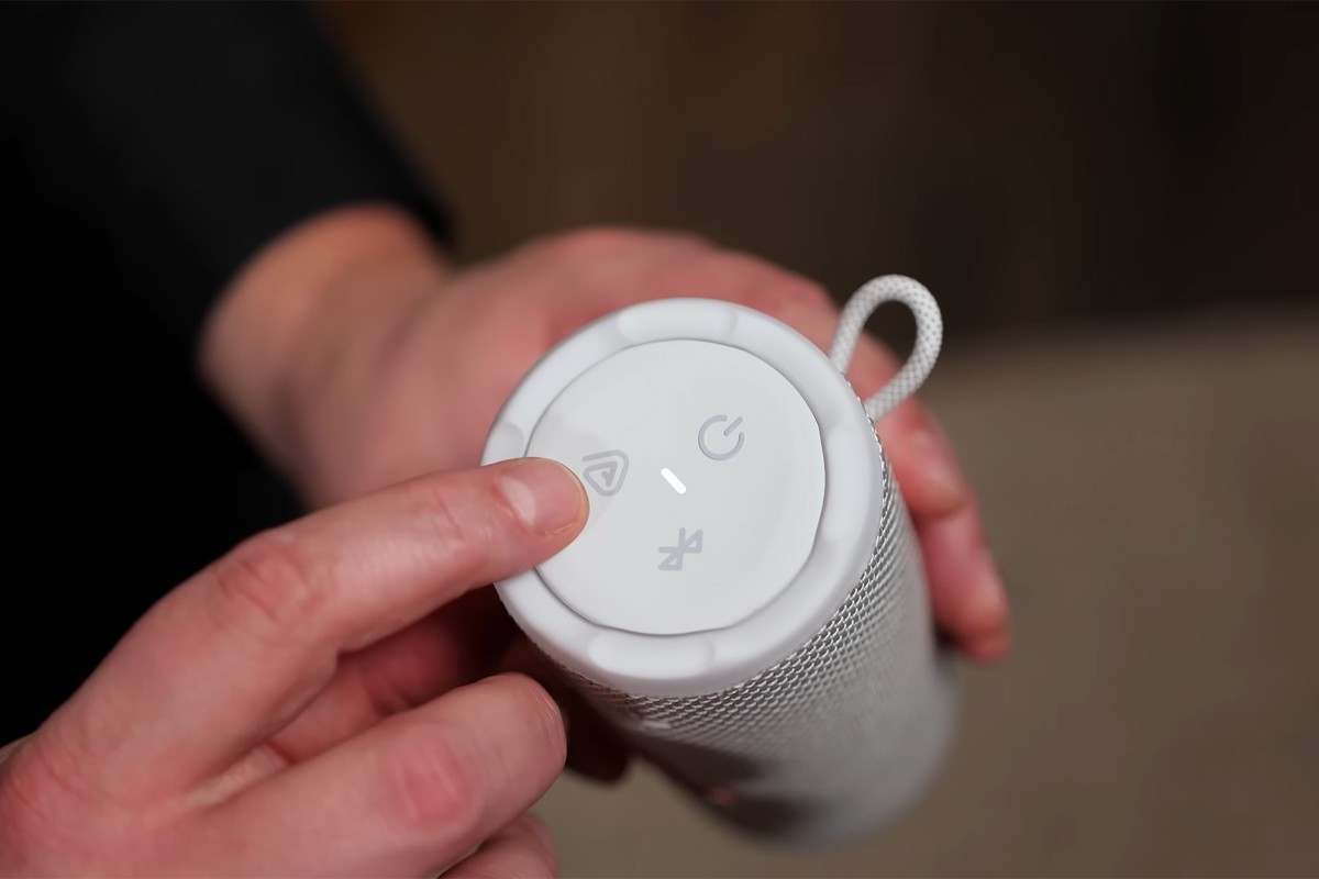 Persoon wijst de bedieningsknoppen op de zijkant van de JBL Grip aan. Zichtbaar zijn de knoppen voor Auracast, Bluetooth en de aan'/uitknop.