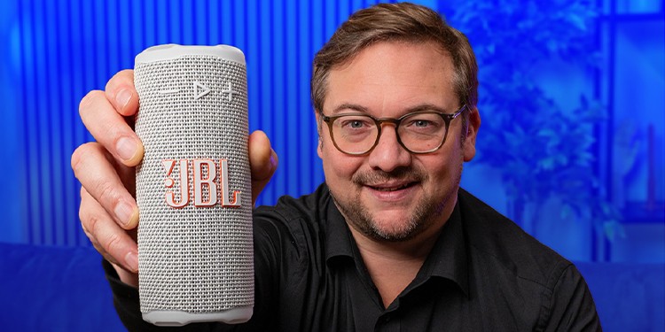 Persoon toont de witte variant van de JBL Grip naar de camera