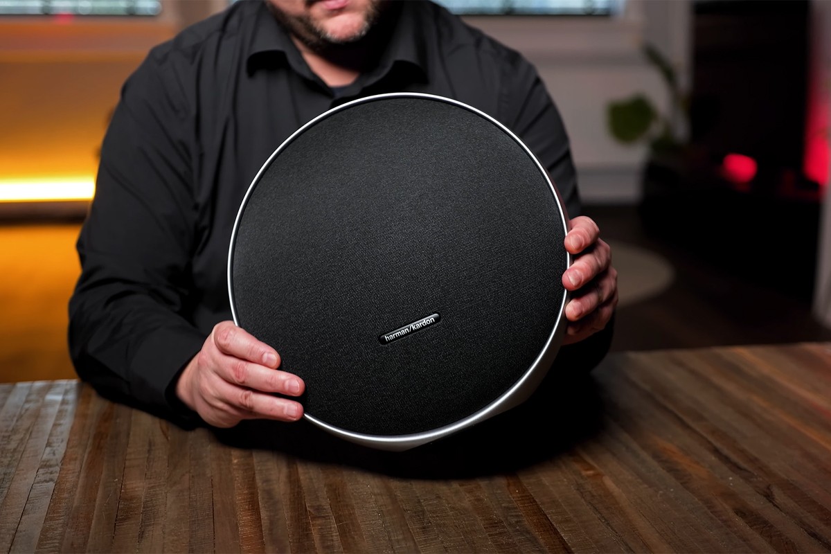Harman Kardon Onyx Studio 9 vastgepakt door een persoon die de speaker aandachtig bekijkt.