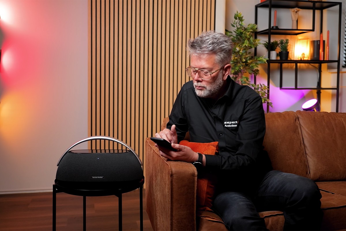 Persoon zit op bank en koppelt telefoon met Harman Kardon Go Play 3 die links naast hem op een tafeltje staat.