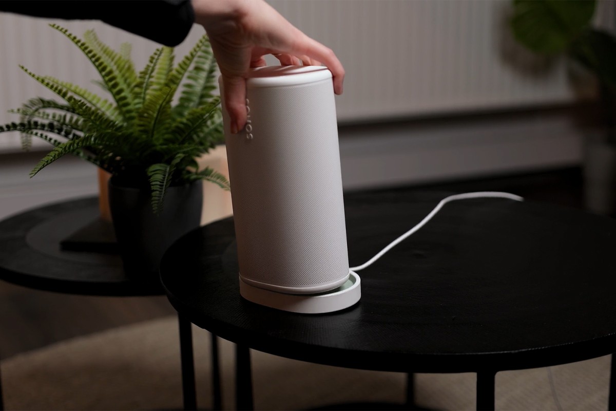 Sonos Play in witte uitvoering wordt door een persoon in het oplaadstation gezet.