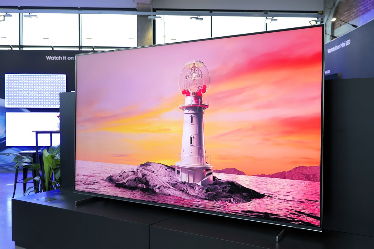 De Samsung R95H staat op opgesteld in een grote showroom. Op het scherm is een beeld te zien van een vuurtoren met een feloranje lucht op de achtergrond.
