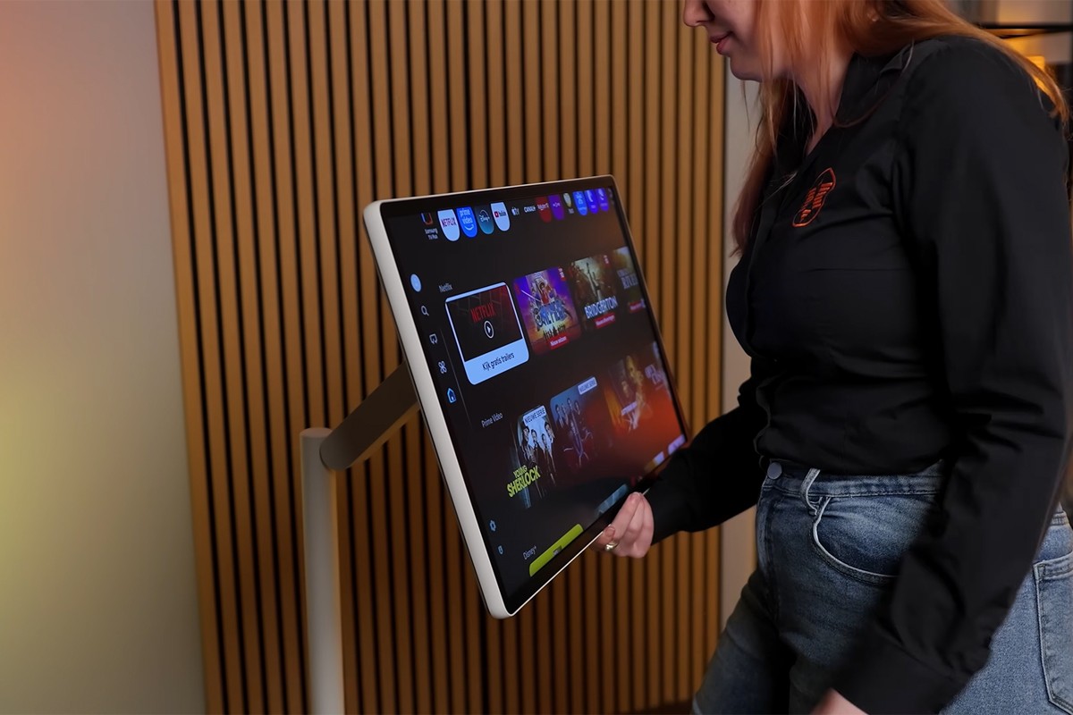 Samsung Movingstyle staat op een standaard en wordt aandachtig bekeken door een vrouw met een zwarte Expert-blouse.