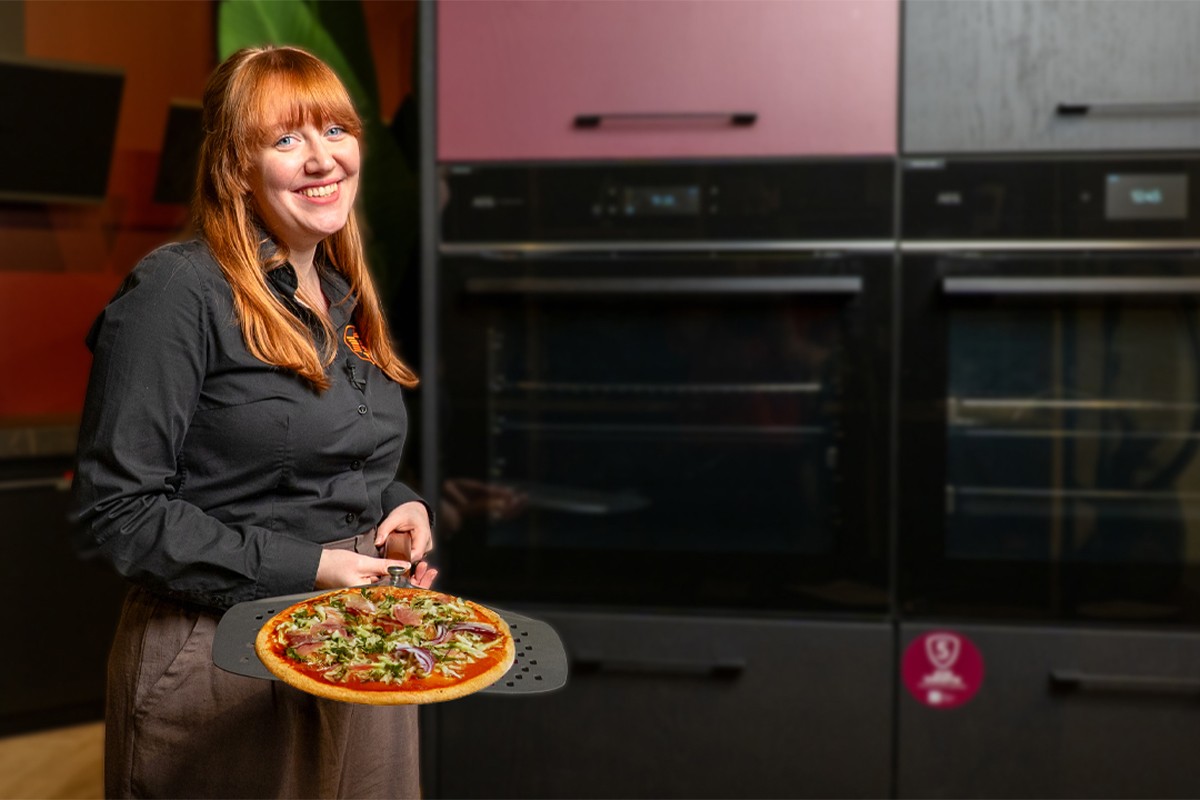 Persoon op voorgrond met pizza op pizzaschep.