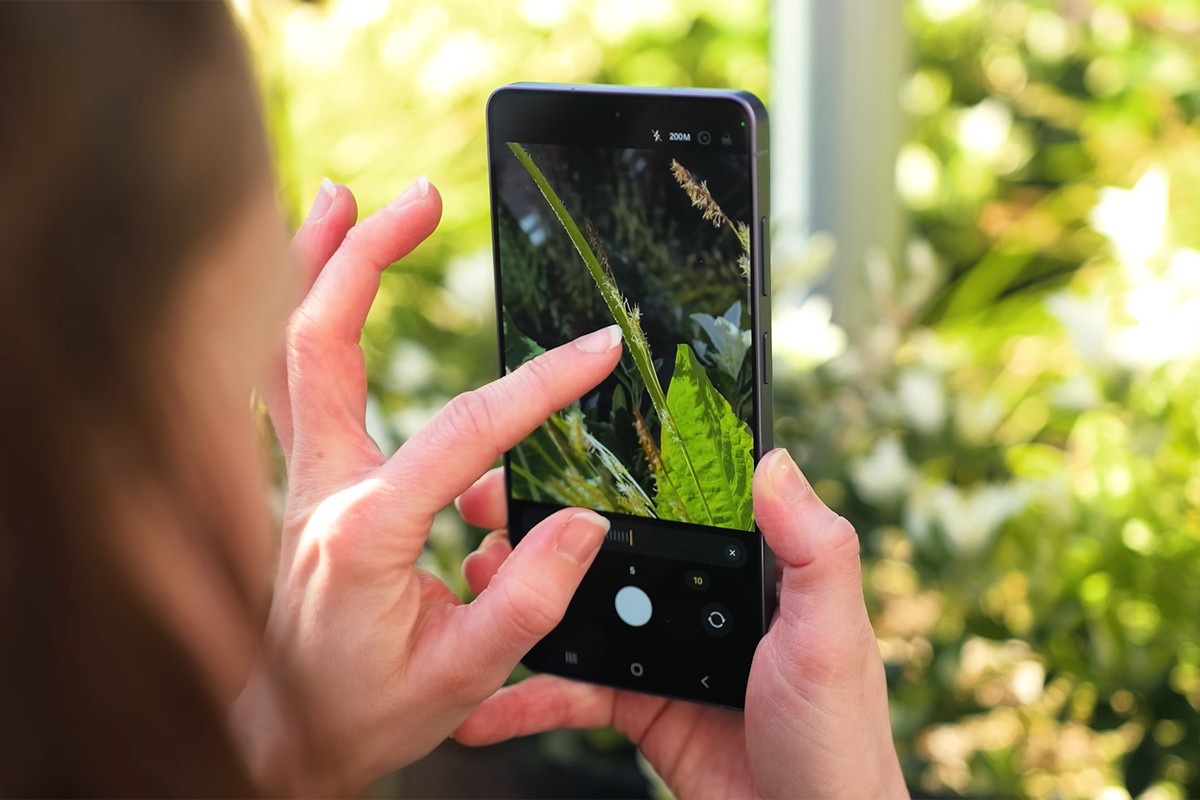 Persoon, geknield bij een plantenbak, maakt een foto met de Samsung Galaxy S26.