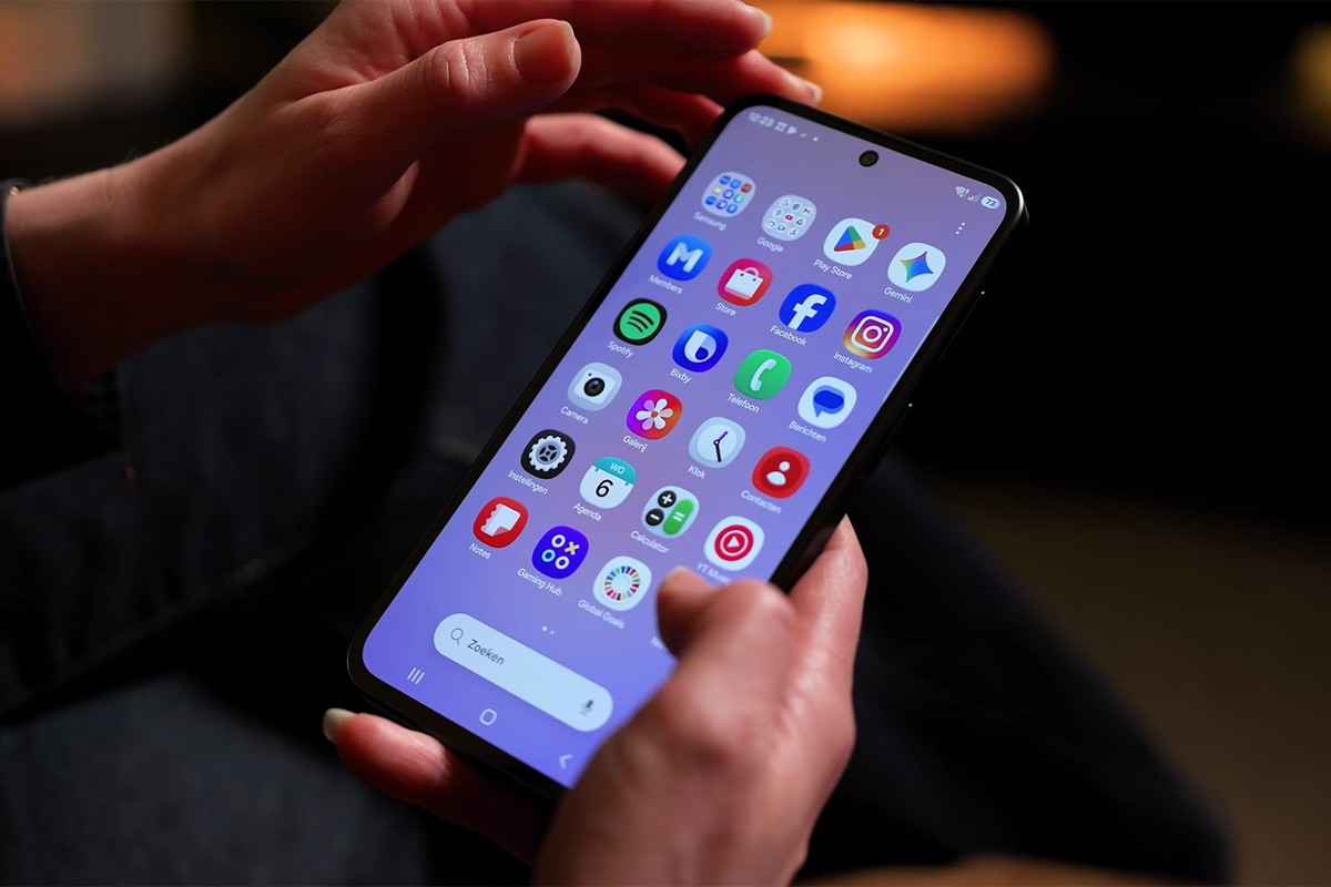 Persoon houdt Samsung Galaxy A37 met beide handen vast. Op het scherm is het startscherm van Android zichtbaar met verschillende apps.