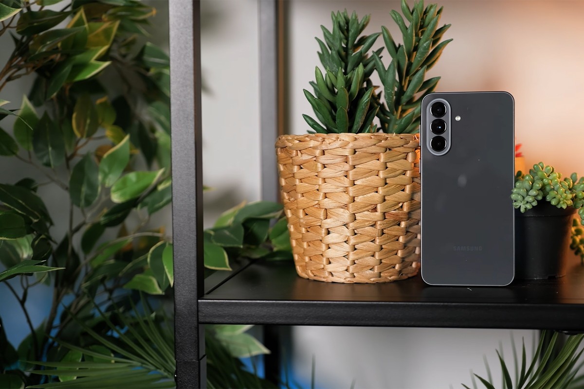 De achterkant van de Samsung Galaxy A37 staat in een kast tussen groene kamerplanten. De drie camera's die verticaal onder elkaar geplaatst zijn, zijn duidelijk zichtbaar.