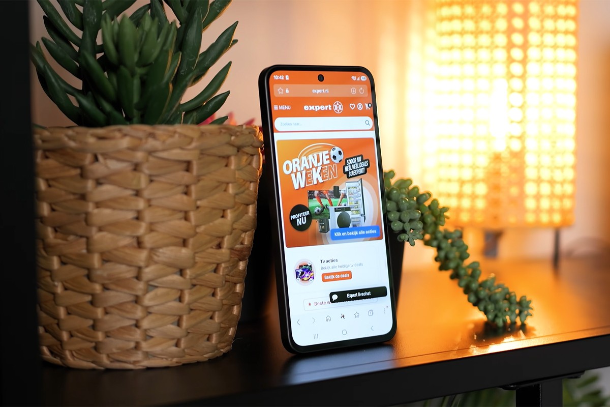 Samsung Galaxy A37 rechtop in een kast, tussen twee kamerplanten. Op het scherm is de website van Expert duidelijk zichtbaar.