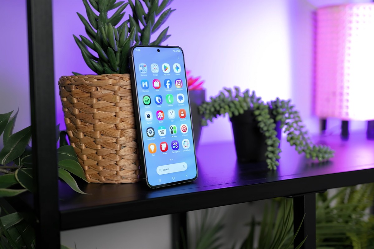 Samsung Galaxy A47 rechtop in een zwarte kast, naast een gevlochten plantenpot met een groene kamerplant. Op het scherm is het Android-startscherm met verschillende apps duidelijk zichtbaar.