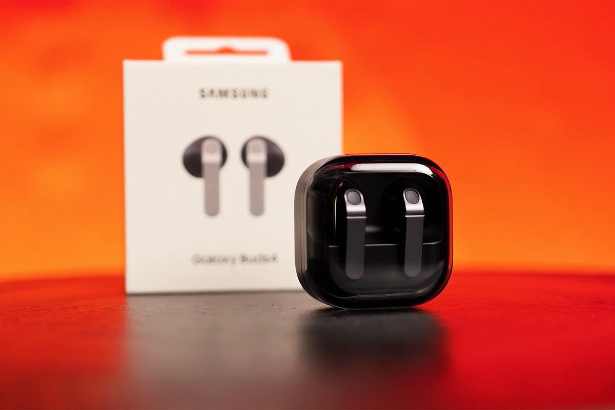 Samsung Galaxy Buds 4 in de oplaadcase met het verpakkingsdoosje en een oranje muur vaag op de achtergrond.