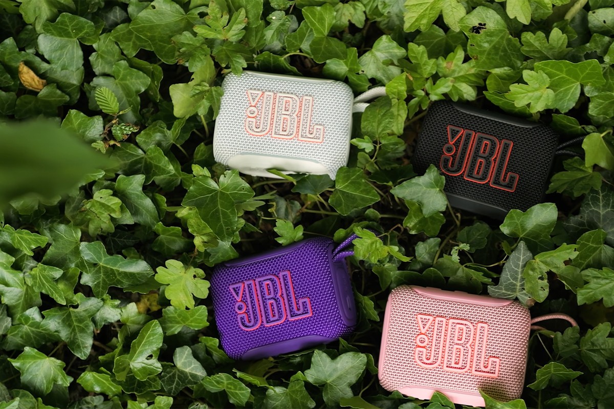 JBL GO 5 speakers in het wit, zwart, paars en roze liggen tussen groene bladeren.