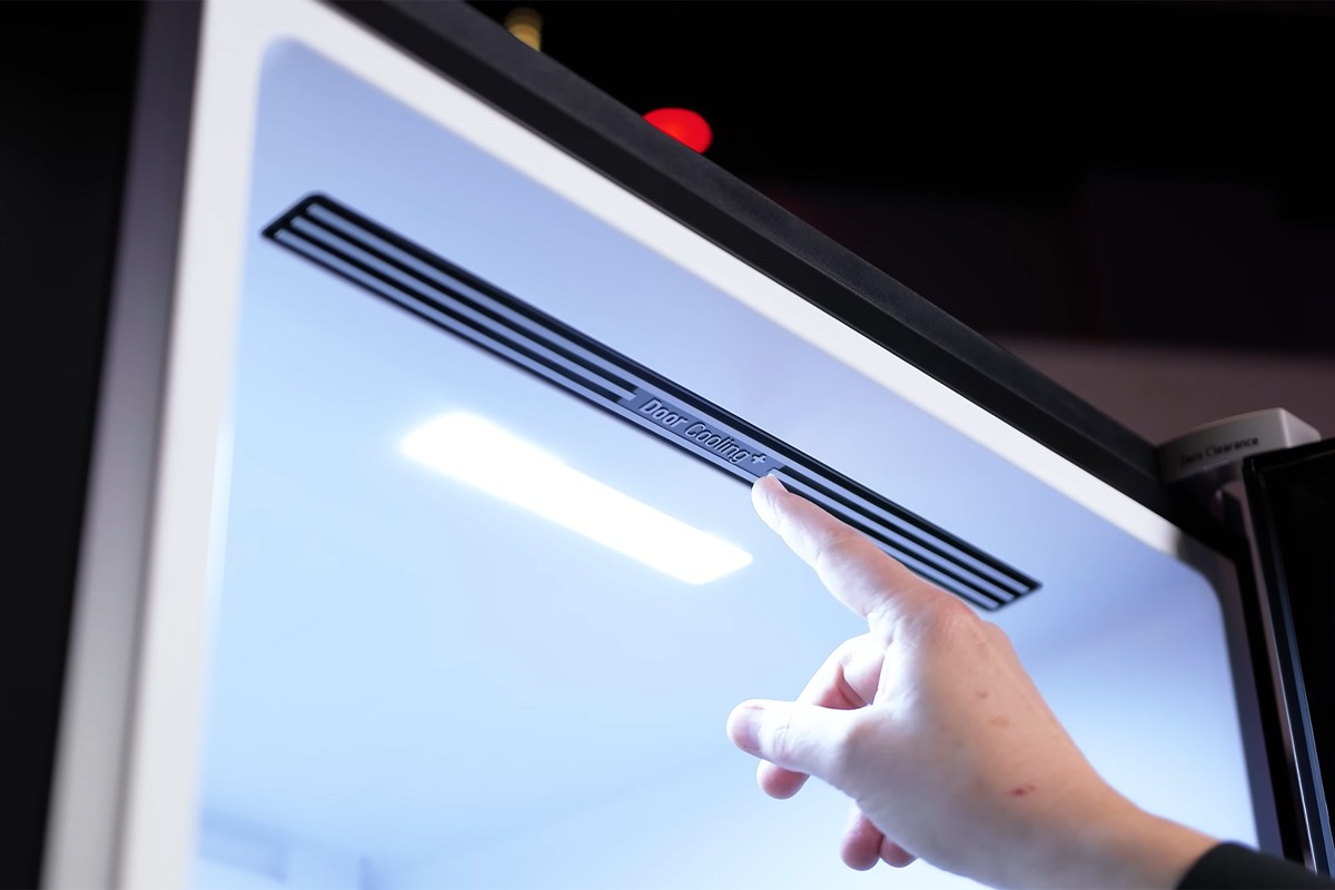 Persoon wijst naar de ventilatieroosters in de bovenkant van de LG Koelkast waar ook de letters van Door Cooling+ te zien zijn.